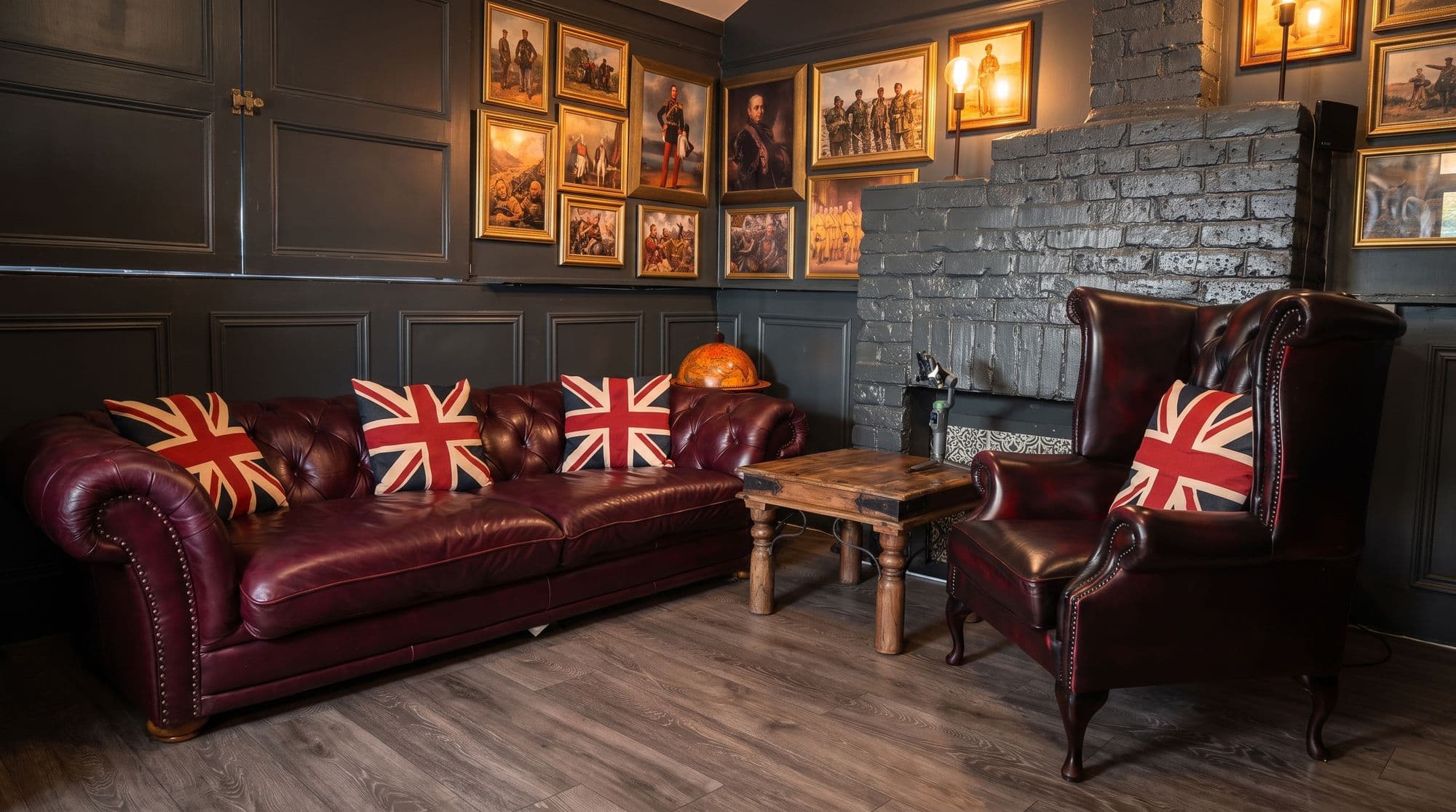 The Anteroom: a Chesterfield sofa and wingback chair with Union Jack cushions, framed military prints and a painted brick fireplace