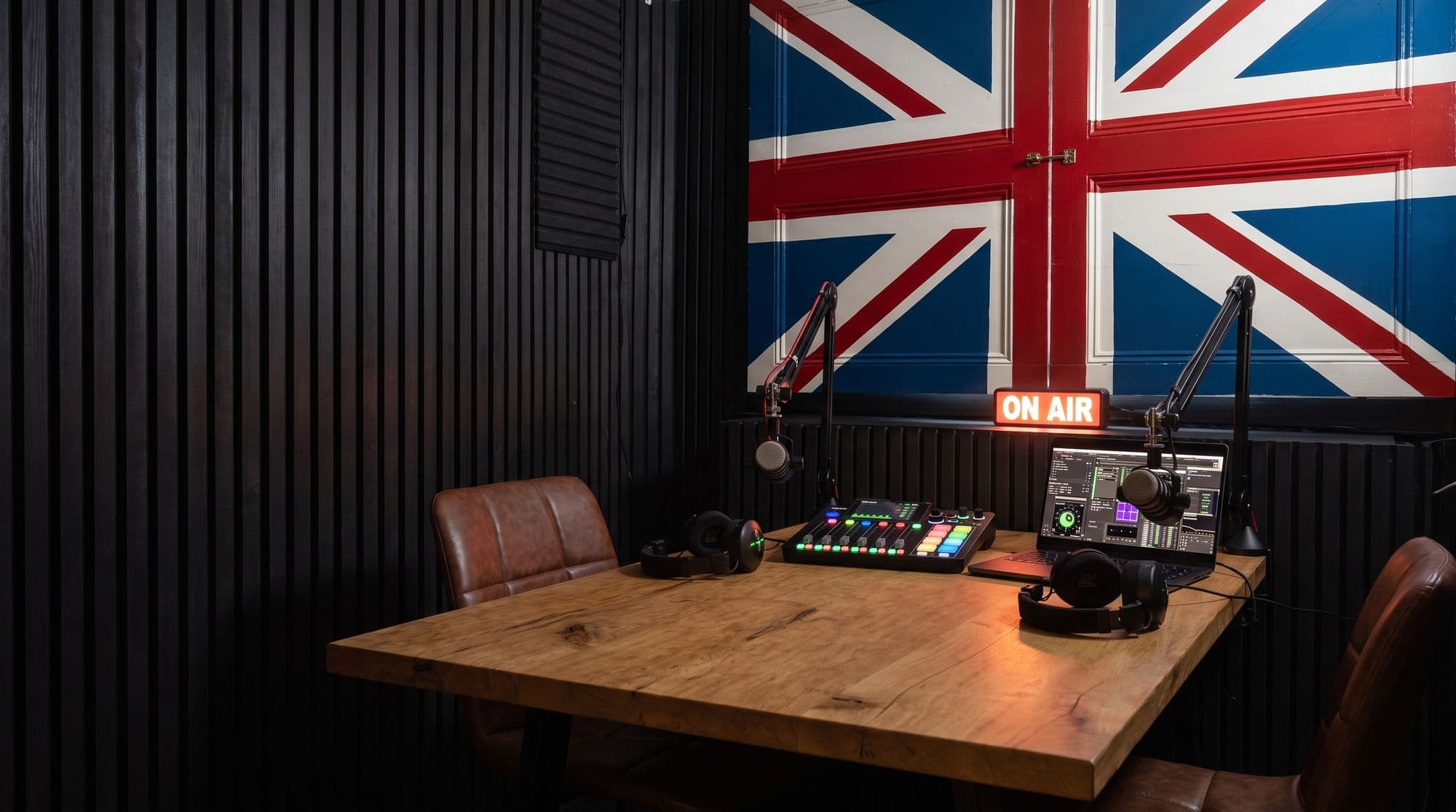 The Signal Room: slatted walls, Union Jack wall, ON AIR sign, and the desk set for two with mics, mixer and headphones